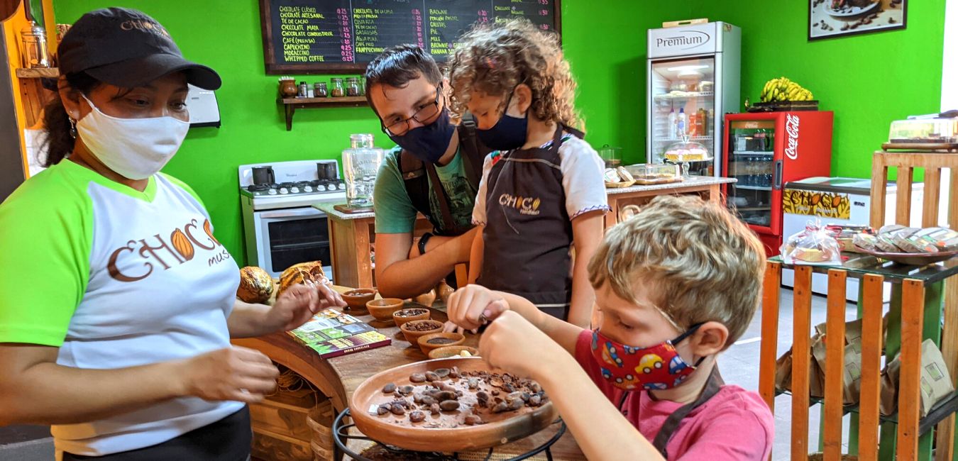 Two kids and their dad look at cacao beans in a clay bowl.