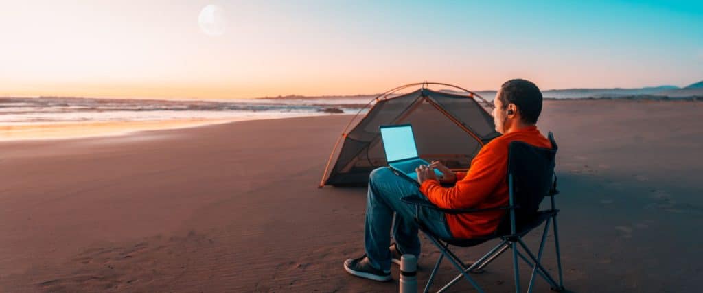 A man works on his laptop while camping on the beach.