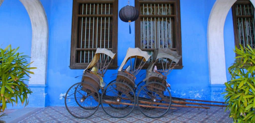 Three trishaws in front of a bright blue wall at the Blue Mansion in Penang. 