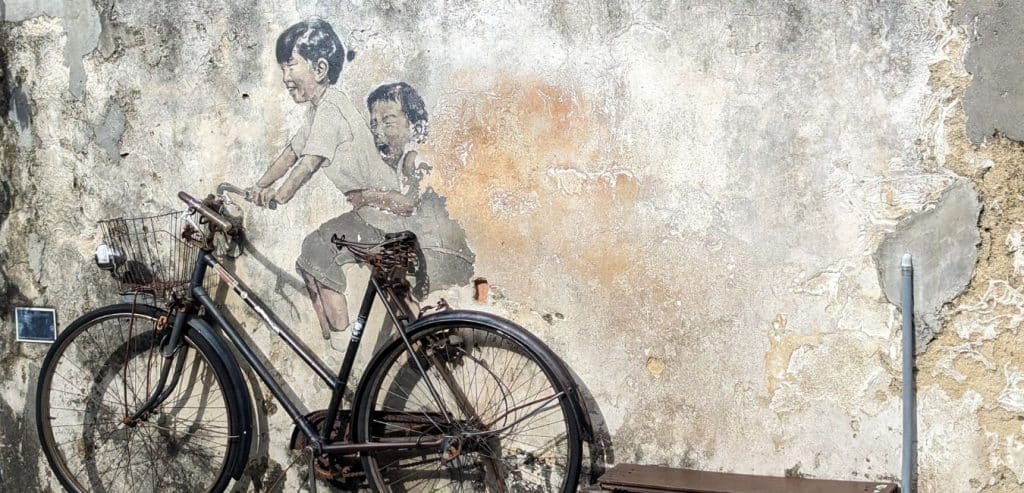 Children painted on a wall in Georgetown appear to be riding a bicycle leaned against the wall.