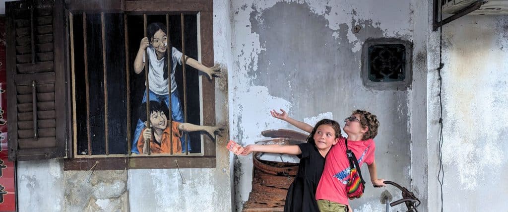 Two kids pretending to interact with a famous street art painting in Georgetown Penang.