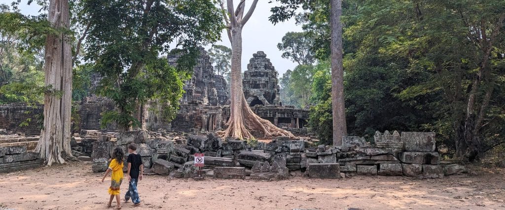 Two kids walking on a jungle path with temple ruins in the background.