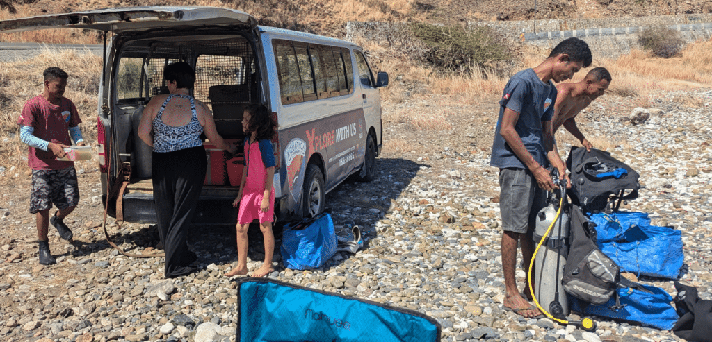 People unloading a van on a stone beach getting ready for a scuba dive.