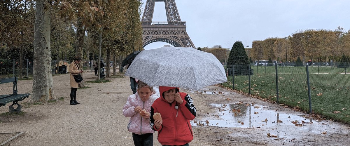 Two kids eating a baguette under an umbrella in front of the Eiffel Tower